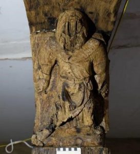 Early 14th century carved man supporting the undercroft axial beam, his face has been hacked off in the Reformation or English Civil War, and he has been scorched with ‘taper burns’ to ward away evil (photo Urban Archaeology)