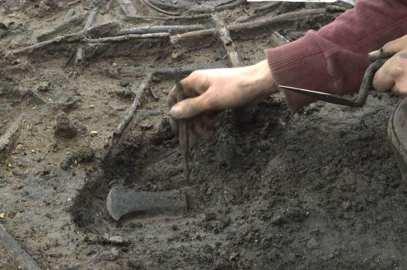 Archaeologist from the Cambridge Archaeological Unit uncovering an axe head during excavations at the Must Farm site in 2016.  Credit: Cambridge Archaeological Unit 